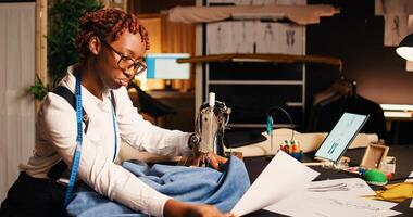 Designer working on sewing machine to manufacture clothing items at workstation, professional tailor. Young couturier using tailoring equipment to create custom made clothes in atelier. photo