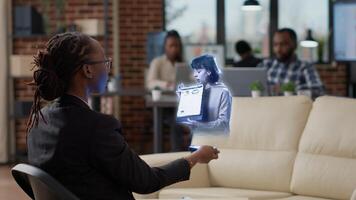 BIPOC employee in augmented reality teleconference meeting in high tech office talking with coworker. Accountant at workplace desk in online videocall with manager using hologram technology photo