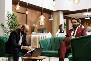 Hotel reception providing good business meeting space with elegant ambiance, entrepreneurs preparing to attend official international meeting. Management team sitting in lounge area at hotel. photo