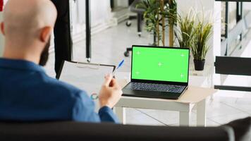 Businessman looks at greenscreen in office, using laptop to plan company strategy. Middle eastern man working on isolated copyspace display, entrepreneurship concept in coworking space. photo