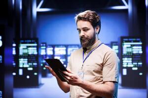 Administrator in front of server rackmounts delivering web content to clients over the internet. Manager in high tech facility using tablet to make sure critical systems are in faultless condition photo