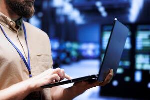 Close up of admin using laptop to check electronics in blockchain technology application specific integrated circuit server rig clusters. Focused employee checking for issues in crypto mining farm photo