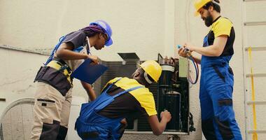 Expert repairmen cleaning layer of dirt and dust from air conditioner compressor coils while coworker uses manifold indicators to check for refrigerant leaks and read pressure in hvac system photo