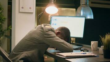 Drowsy african american computer operator asleep in desk chair while working overnight in office. Tired employee taking a nap at work, alone in workspace with tasks left unfinished photo