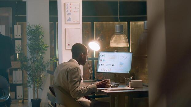 Employee enjoying cup of coffee while imputing financial datasets on computer during nightshift, helped by supervisor. Accountant working in office under manager guidance photo