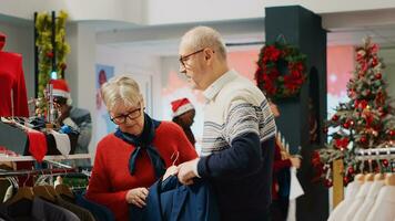 mujer hojeada mediante Navidad adornar ropa Tienda bastidores con marido en Navidad compras juerga. mayor Pareja buscando para elegante atuendo vestidos como regalo para hijo durante invierno fiesta temporada foto