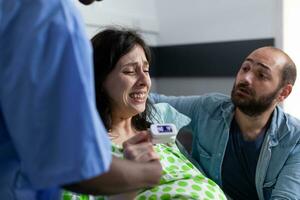 Pregnant woman holding hand of nurse and husband in hospital ward, having painful contractions. Patient with pregnancy getting into labor having medical assistance at healthcare facility. Close up photo