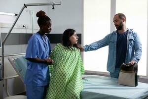 African american obstetrics nurse helping pregnant woman to get out of bed in hospital ward, preparing patient for caesarean surgery. Future parents expecting child in maternity clinic photo