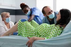 Pregnant woman delivery baby in hospital ward, medical team and husband comforting patient with contractions during caesarean surgery. Future mother giving birth to child in maternity clinic photo