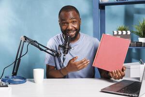 African american blogger promoting new book and showing red cover mockup while recording video for internet channel. Author presenting new novel while streaming for online blog photo
