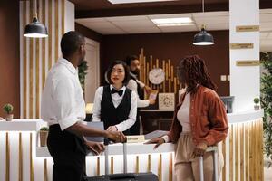 Hotel employee registering people at front desk, using computer to review room reservation and booking details. Receptionist welcoming guests in luxury resort, check in register. photo