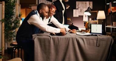 Two couturiers cutting material for modern clothing items in workshop, using scissors on fabric for handcrafting atelier process. Team of designers preparing for tailoring and needlework. photo