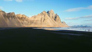 zumbido Disparo de Stokksnes negro arena playa en Islandia, hermosa vestrahorn montañas en nórdico escenario. espectacular islandés naturaleza con Oceano línea costera, atlántico costa. lento movimiento. foto