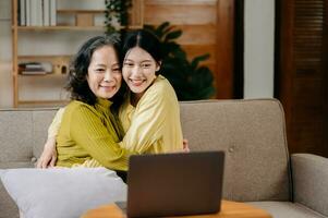 Happy adult granddaughter and senior grandmother having fun enjoying talk sit on sofa in modern living room, using a laptop, tablet bonding chatting relaxing at home together photo