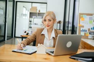 Young real estate agent worker working with laptop and tablet at table in office and small house beside it. photo