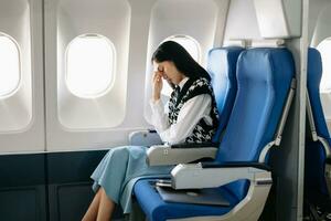 Photo of a frustrated woman sitting on an airplane with her head in her hands. Asian woman sitting in a seat