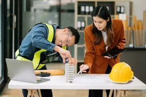 Contractor and architect looking at plan, tablet, laptop and talking about working on big project. Building in construction office interior. photo