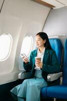 retrato de exitoso asiático mujer de negocios o empresario en un formal traje en un avión sentado en negocio clase utilizando un teléfono, computadora ordenador portátil. viaje en estilo, trabajo con gracia. foto