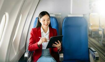 retrato de exitoso asiático mujer de negocios o empresario en un formal traje en un avión sentado en negocio clase utilizando un teléfono, computadora ordenador portátil. viaje en estilo, trabajo con gracia. foto