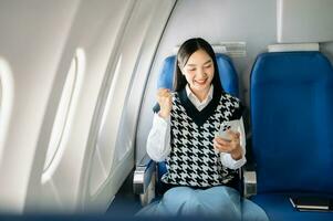 Attractive Asian female passenger of airplane sitting in comfortable seat while working laptop and tablet with mock up area using wireless connection. Travel in style, work with grace. photo