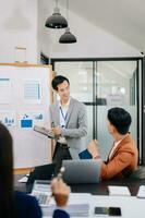 The boss stands near the board with graphs, demonstrates statistics, various personnel attending the training, introduces the new products of the company, in office photo