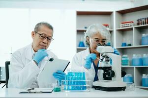 Two scientist or medical technician working, having a medical discuss meeting with Asian senior female scientist supervisor in the laboratory with online reading, test samples and innovation photo