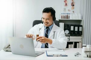 Attractive male doctor talking while explaining medical treatment to patient through a video call with laptop in office photo