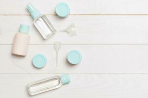 Top view composition of small travelling bottles and jars for cosmetic products on wooden background. Facial skin care concept with copy space for your design photo