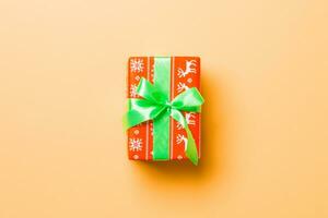 wrapped Christmas or other holiday handmade present in paper with green ribbon on orange background. Present box, decoration of gift on colored table, top view with copy space photo