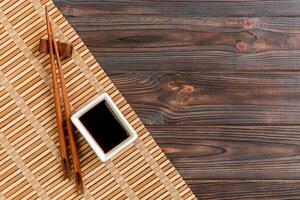 Bamboo mat and soy sauce with sushi chopsticks on wooden table. Top view with copy space background for sushi. Flat lay photo