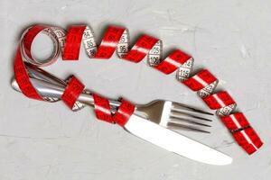 Diet concept with fork, knife and measuring tape on gray background. Top view of weight loss photo