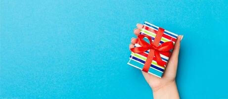 Woman arms holding gift box with colored ribbon on blue table background, top view and copy space for you design photo