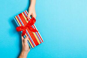 Top view of holding a gift in female and male hands on colorful background. Woman and man give and receive a present. Time for holiday concept with copy space photo