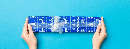 Woman arms holding gift box with colored ribbon on blue table background, top view and copy space for you design photo