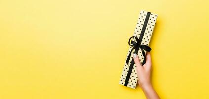 mujer brazos participación regalo caja con de colores cinta en amarillo mesa fondo, parte superior ver y Copiar espacio para usted diseño foto