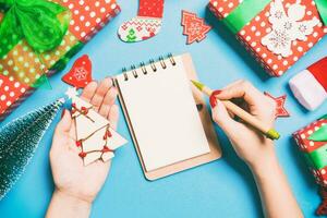 Top view of female hand making some notes in noteebok on blue background. New Year decorations and toys. Christmas time concept photo