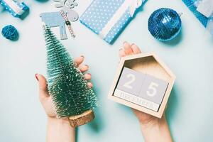 Top view of female hands holding calendar on blue background. The twenty fifth of December. Holiday decorations. Christmas time concept photo