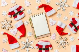 Top view of notebook with Christmas decorations and Santa hats on orange background. Happy holiday concept photo