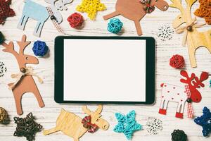 Top view of tablet on holiday wooden background. New Year decorations and toys. Christmas concept photo