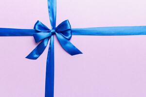 Top view of blue ribbon rolled and blue bow isolated on colored background. Flat lay with copy space photo