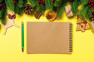 vista superior del cuaderno sobre fondo amarillo hecho de adornos navideños. concepto de tiempo de año nuevo foto