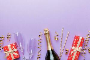 Bottle of champagne with colored glitter, confetti and gift box space for text on colorfull background, top view. Hilarious, christmas and birthday celebration photo