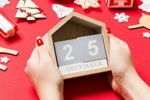 Top view of female hands holding calendar on red background. The twenty fifth of December. Holiday decorations. Christmas time concept photo