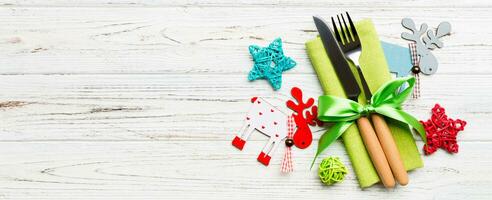 Banner New Year set of fork and knife on napkin. Top view of christmas decorations and reindeer on wooden background. Holiday family dinner concept with empty space for your design photo