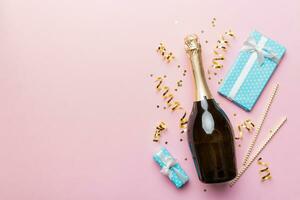 Bottle of champagne with colored glitter, confetti and gift box space for text on colorfull background, top view. Hilarious, christmas and birthday celebration photo