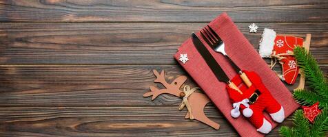 Banner top view of holiday objects on wooden background. Utensils tied up with ribbon on napkin. Christmas decorations and reindeer with copy space. New year dinner concept photo