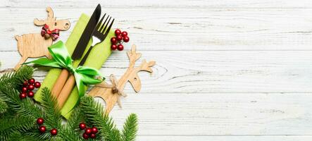 Banner top view of holiday objects on wooden background. Utensils tied up with ribbon on napkin. Christmas decorations and reindeer with copy space. New year dinner concept photo