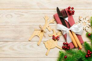 Top view of holiday objects on wooden background. Utensils tied up with ribbon on napkin. Christmas decorations and reindeer with copy space. New year dinner concept photo