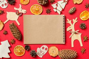 Top view of notebook, red background decorated with festive toys and Christmas symbols reindeers and New Year trees. Holiday concept photo