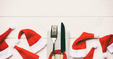 Festive set of fork and knife on wooden background. Top view of new year decorations and santa clothes and hat. Christmas concept with copy space photo